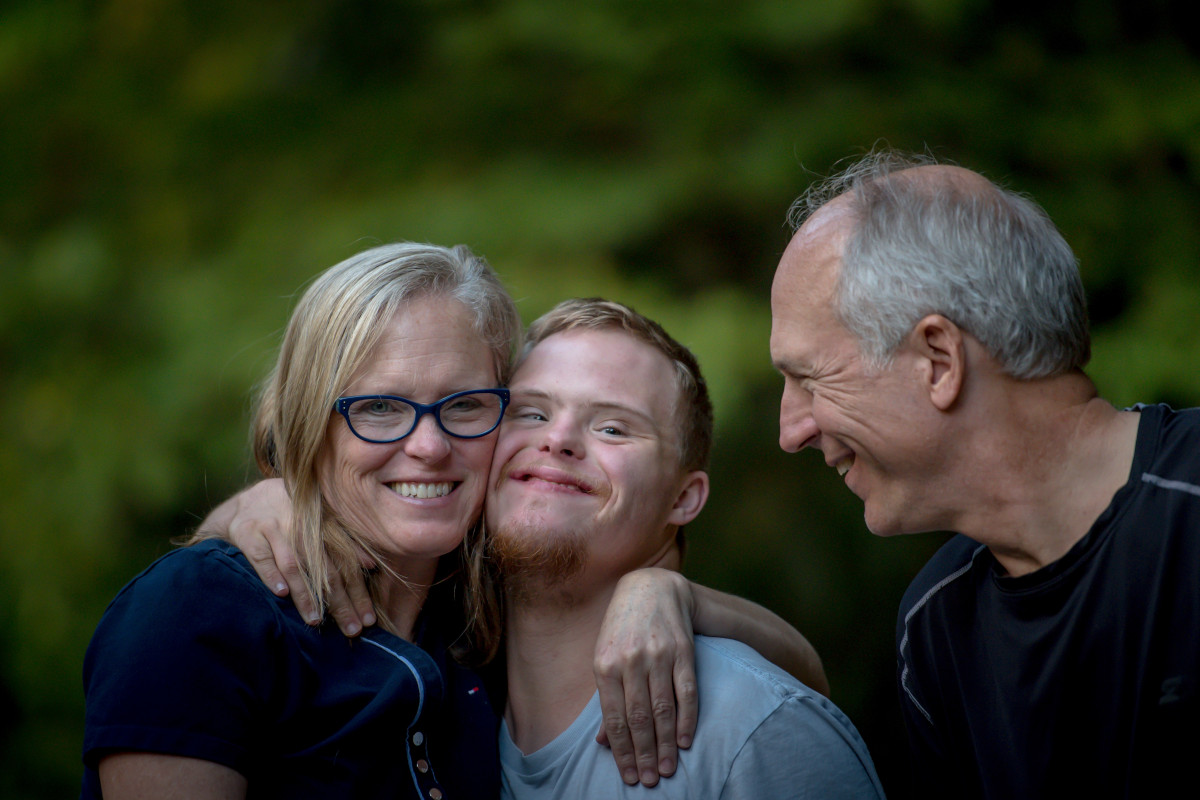 Three people embracing outdoors with green foliage in the background.