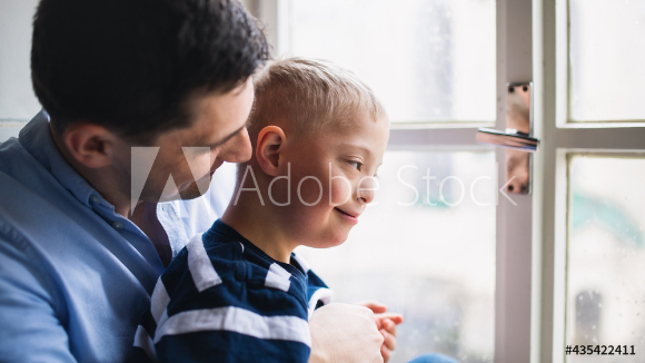 An adult and a child are standing near a window, looking outside.