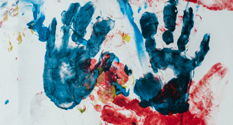 A white background with two handprints in blue and dark blue ink, and red and yellow paint splatters around them.