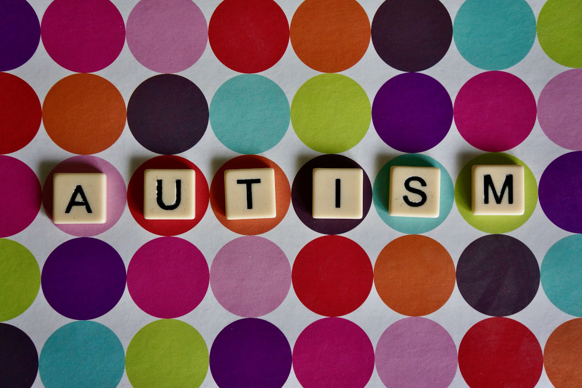 White letter tiles spelling AUTISM on a background of colorful circular shapes.