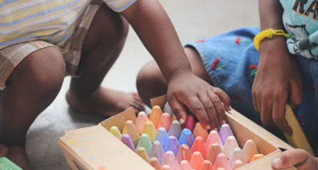 Two children interacting with a box of multicolored chalks.
