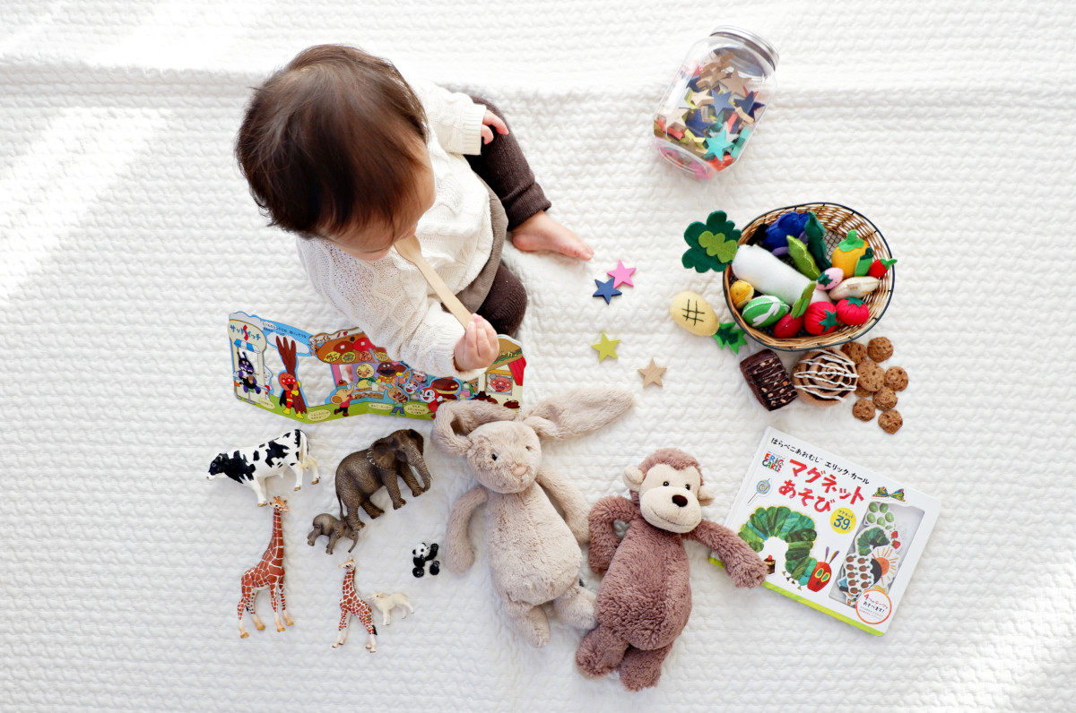 A baby is sitting on a white blanket with various toys around them.